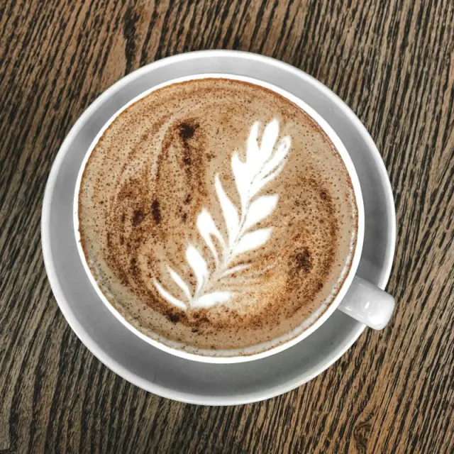 A flat white with leaf latte art on a wooden café table.