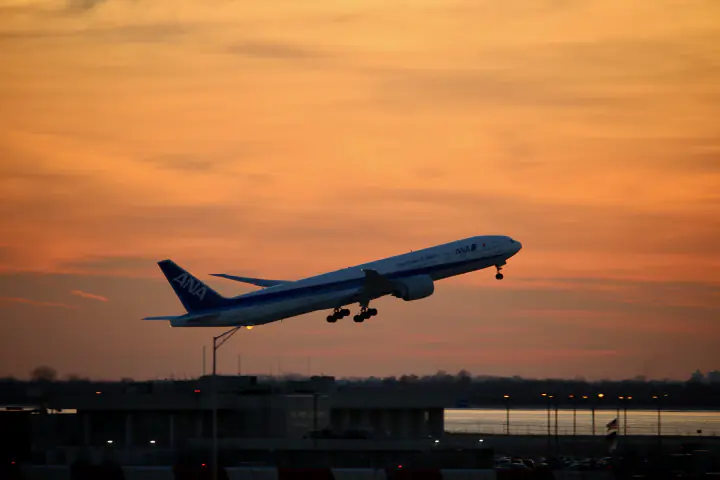 A passenger jet taking off into an orange sunset sky.